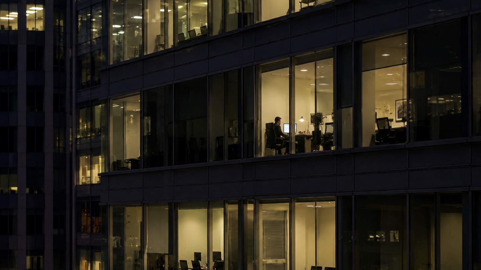 Office building at night, one employee working late while the systems around them keep running unattended